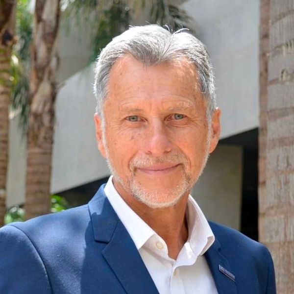 Smiling mature man in a blue suit outdoors with palm trees.