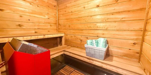 Cozy wooden sauna interior with a red heater and green towels.