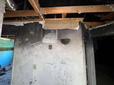 Interior wall with fire damage and exposed ceiling beams.