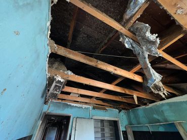 Room with a severely damaged ceiling showing charred wood and torn insulation.