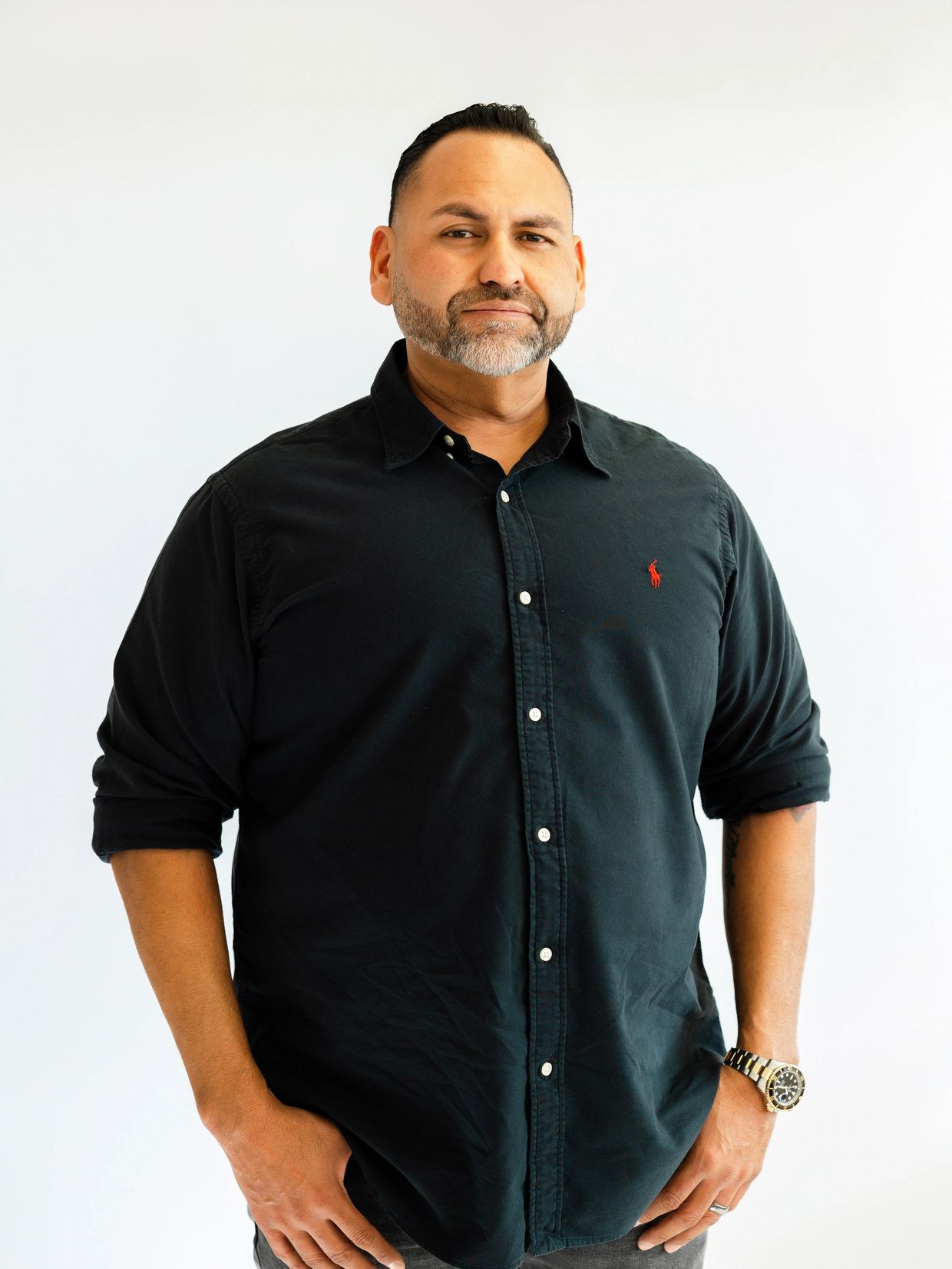 Man in a black shirt with rolled-up sleeves standing confidently.