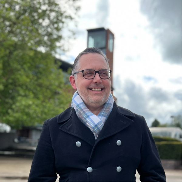 Man smiling outdoors in a scarf and coat.