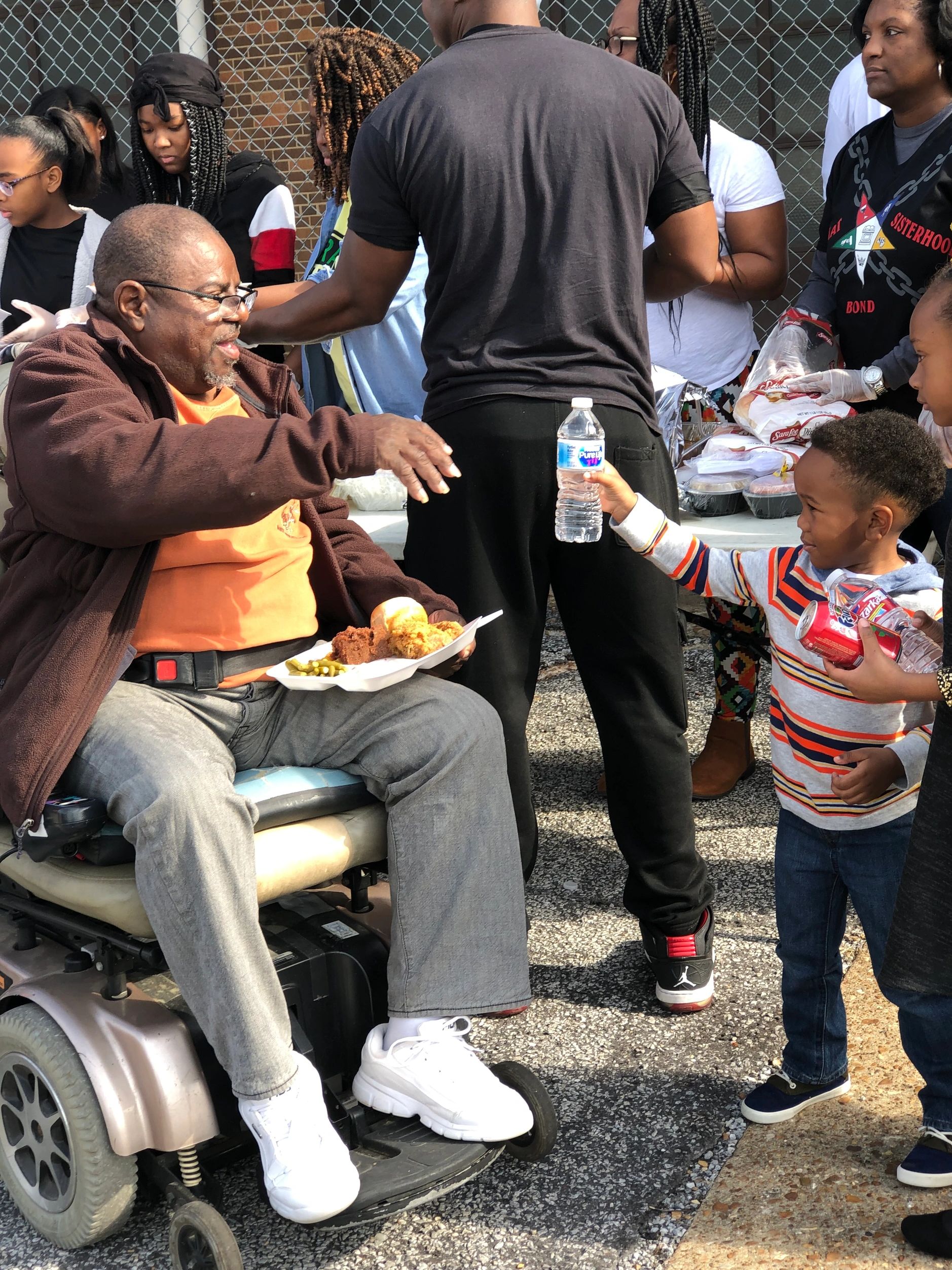 Boy offers water bottle to elderly man in wheelchair.