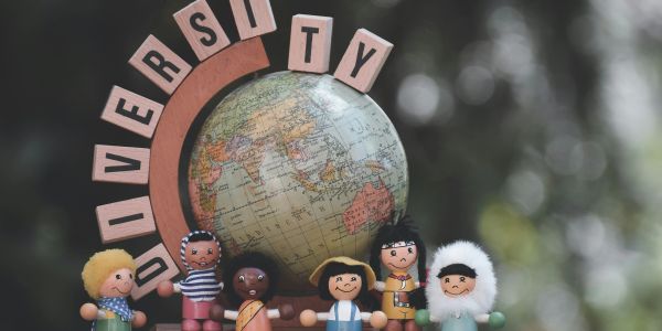 Wooden dolls representing diversity in front of a globe with letter blocks.