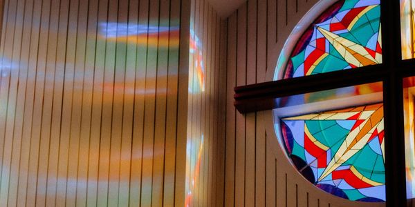 Stained glass window casting colorful light reflections on a wooden wall.