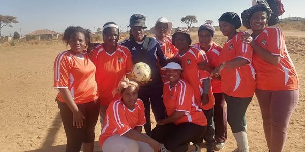 A group of women in orange sports jerseys posing with a soccer ball outdoors.