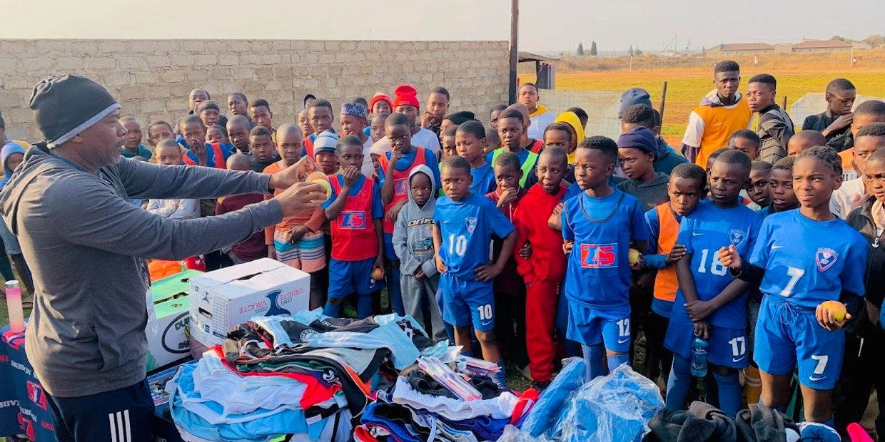 Coach distributing soccer gear to eager young players in a community field.