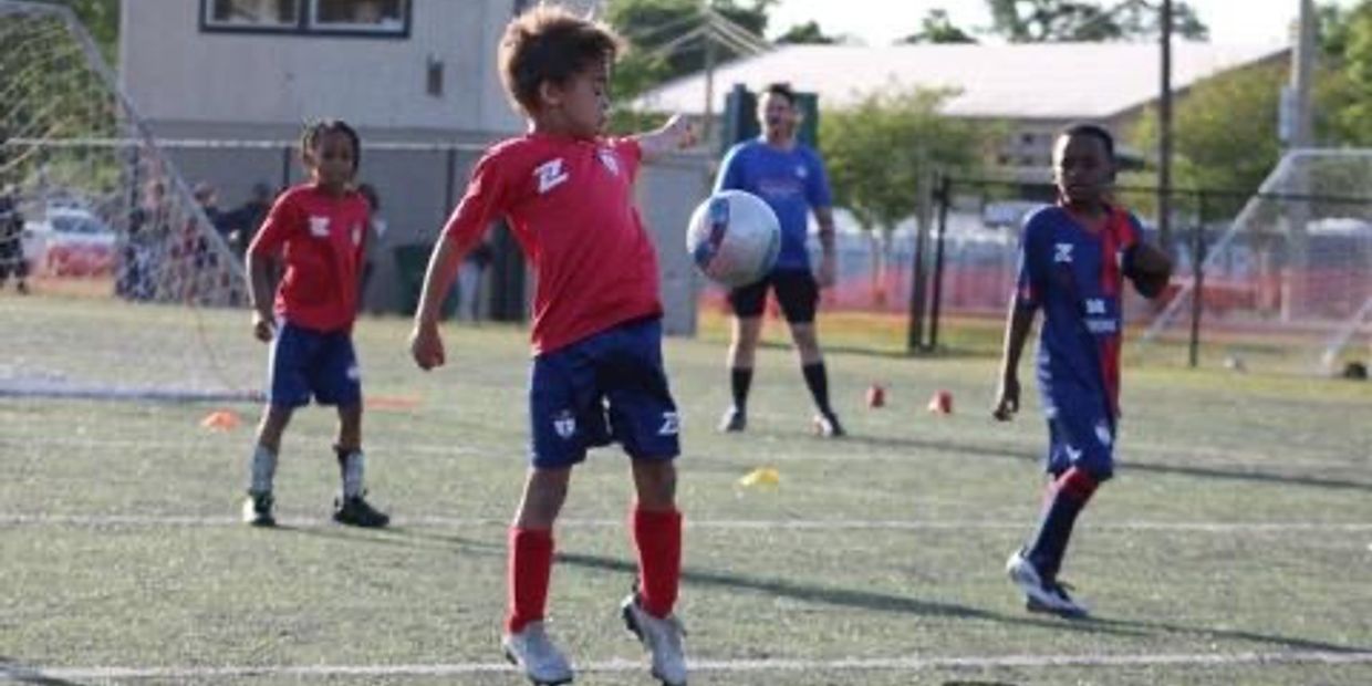 Young kids playing soccer on a field during a sunny day.