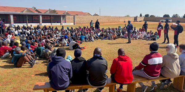 Large group gathered outdoors for a community meeting or event with speakers addressing them.