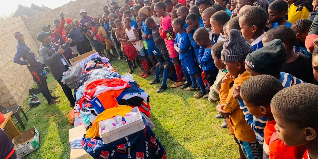 Children gathered around tables with sportswear and supplies, listening to a speaker.