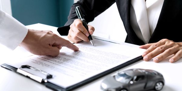 A vehicle dealer with a client signing some car documents