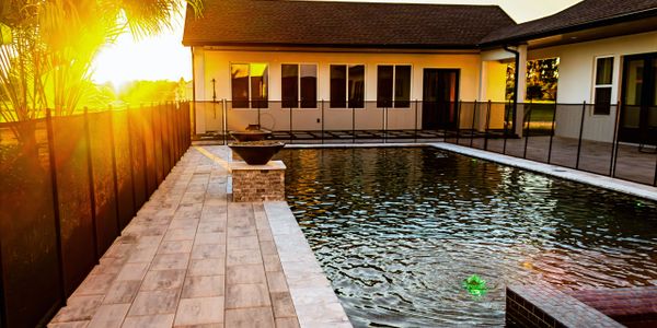 A backyard pool at sunset with modern fencing and tiled patio.