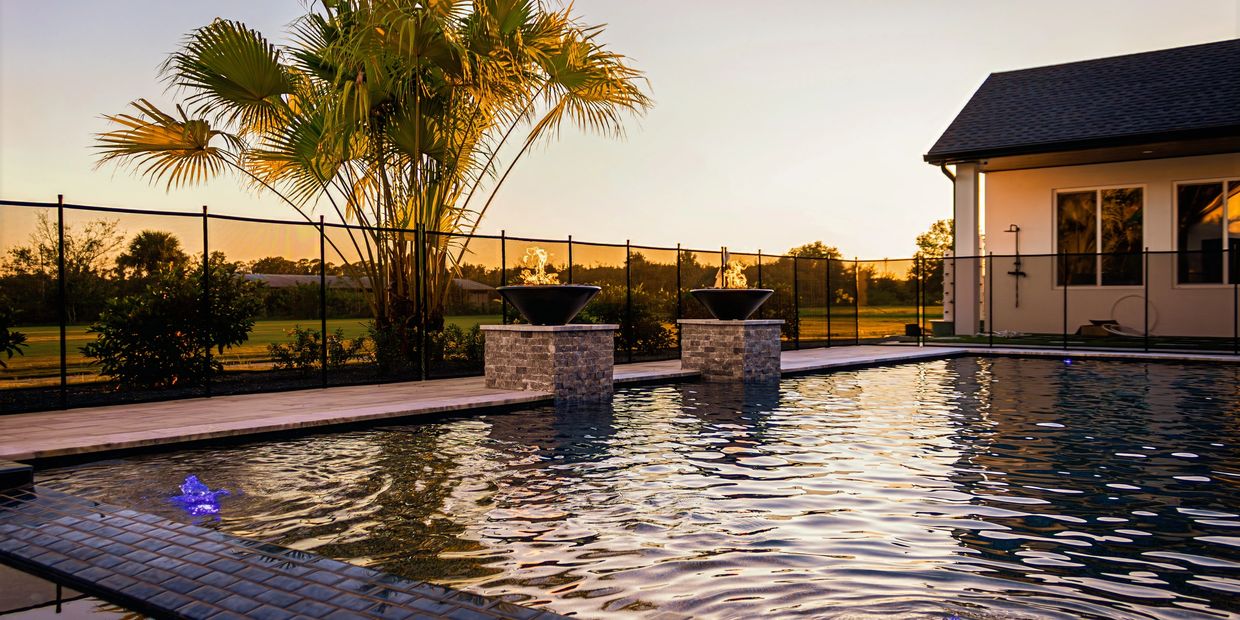 A serene backyard pool at sunset with fire features and palm trees.