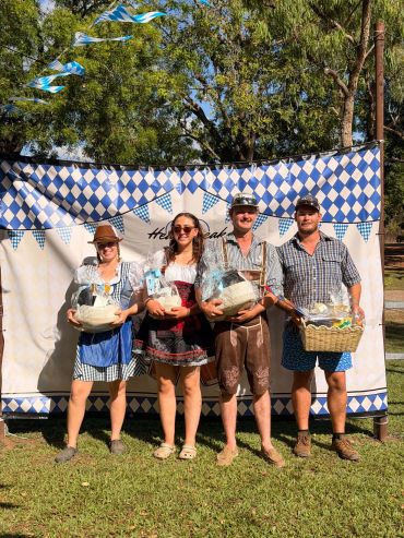 Group in Bavarian outfits holding gift baskets outdoors.