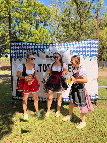 Three women in traditional Oktoberfest dresses holding drinks outdoors.