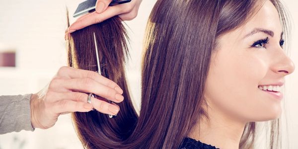 A woman smiling as her hair is being trimmed at a salon.