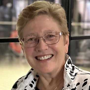 Smiling woman wearing glasses and a patterned blouse.