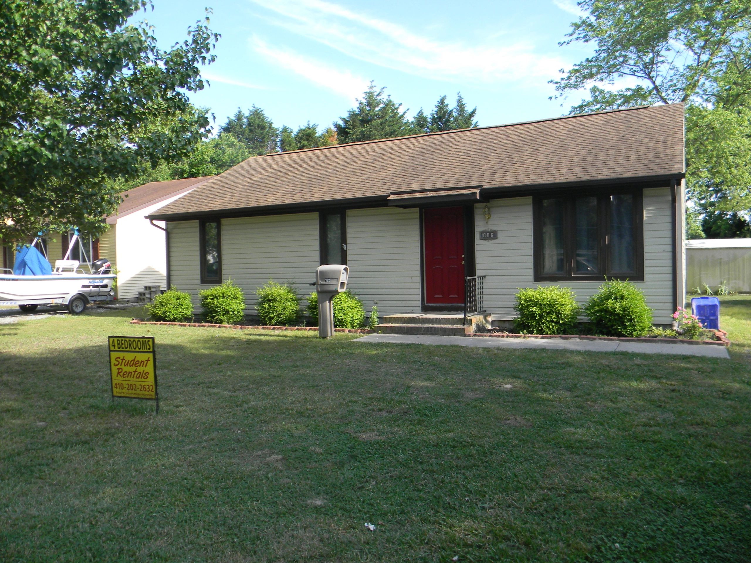 Single-story house with a red door and a boat in the yard.
