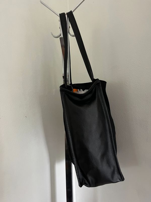 Black leather bag hanging on a coat rack against a plain wall.