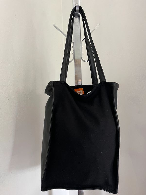 Black tote bag hanging on a metal stand.