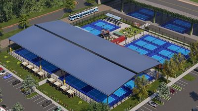 A large sports complex with multiple blue courts and a bus nearby.