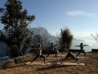 Group practicing yoga outdoors at sunrise with mountains in the background.