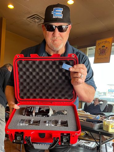 Man in sunglasses holding a red case with glassware and a bottle inside.