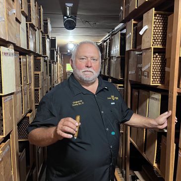 Man holding a cigar in a walk-in humidor filled with cigars.