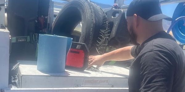 Man working on the back of a service truck under clear blue sky.