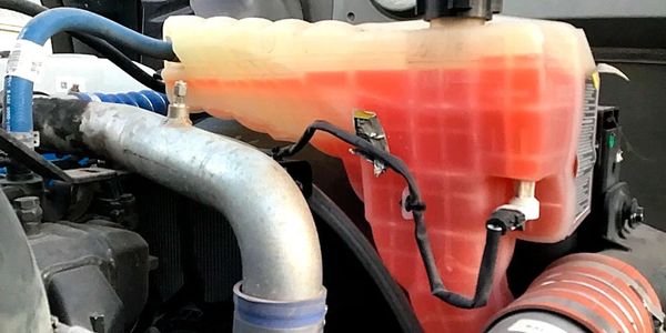 Close-up of a vehicle's engine coolant reservoir with orange coolant inside.