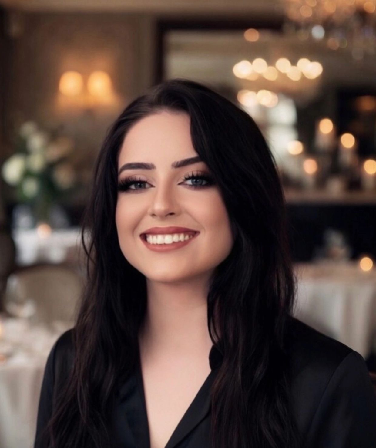 Smiling woman with long dark hair in a dimly lit elegant room.