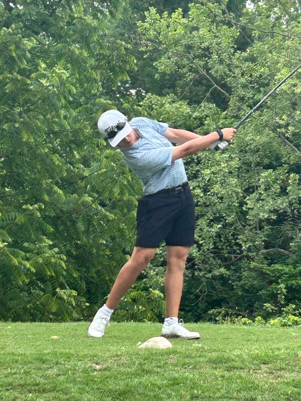 Young man swinging a golf club on a lush green course.
