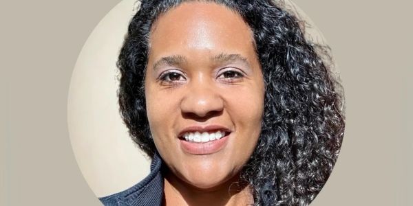 Smiling woman with curly hair and a brown jacket.