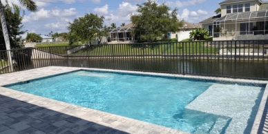 Clear blue backyard swimming pool with a paved deck.