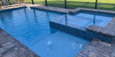 Outdoor swimming pool with attached spa and stone tiles.