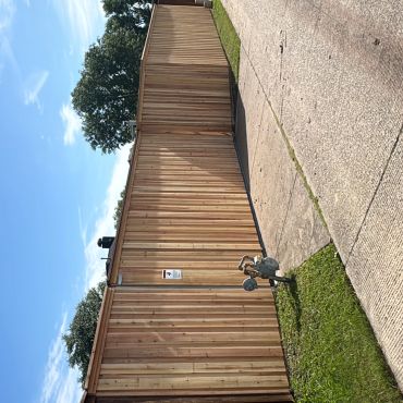 A wooden fence with a lock and a paved pathway beside it under a blue sky.
