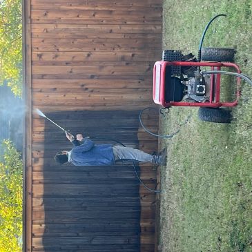 A person power washing a wooden fence, cleaning one side.