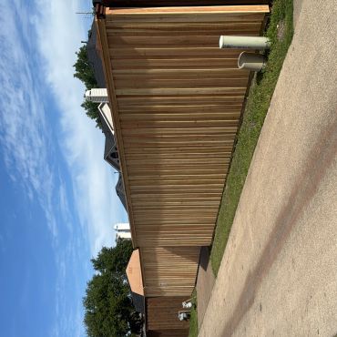 Long wooden fence along a paved pathway under a blue sky.