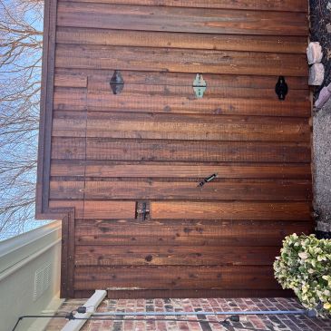 Wooden fence with a hidden door near a brick house and some bushes.