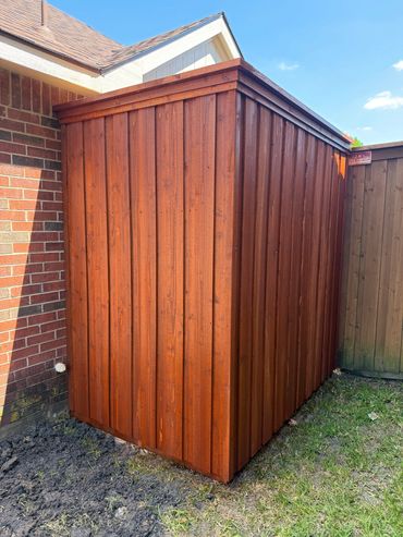 A wooden shed with a red-brown finish against a brick wall in a backyard.
