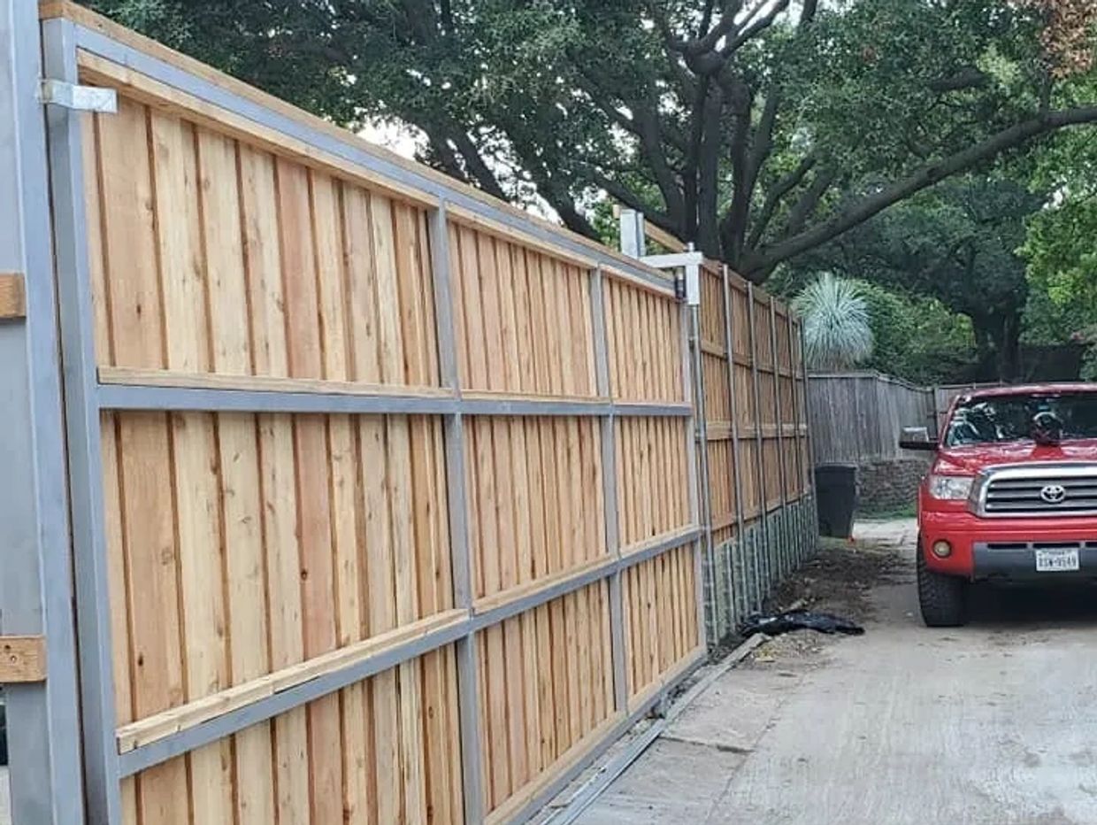 New wooden fence with metal frame alongside a driveway and red Toyota truck.