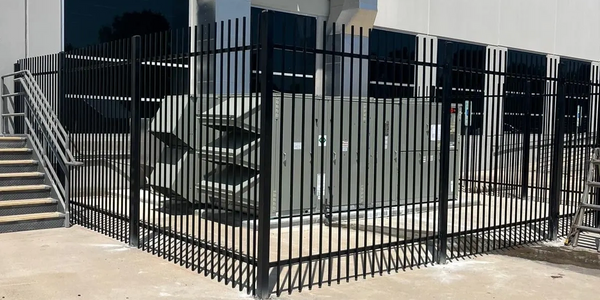 Black metal fence enclosing a utility area outside a building.