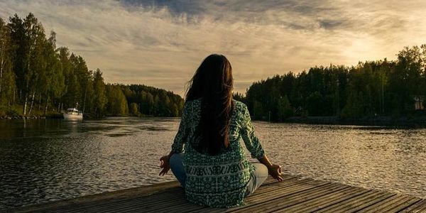 A woman meditating on a dock by a calm lake during sunset.
