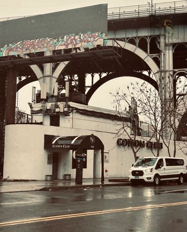 Cotton Club exterior under a bridge with a parked white van on a rainy day.