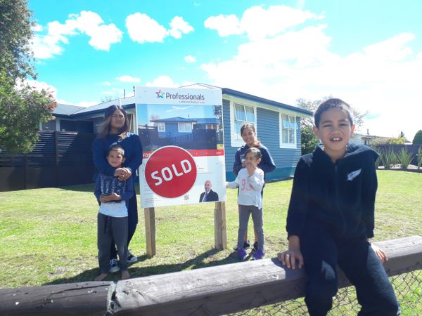 Family celebrates buying a new home with a sold sign in front.