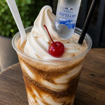 A creamy frozen drink with cherry and vodka bottle.