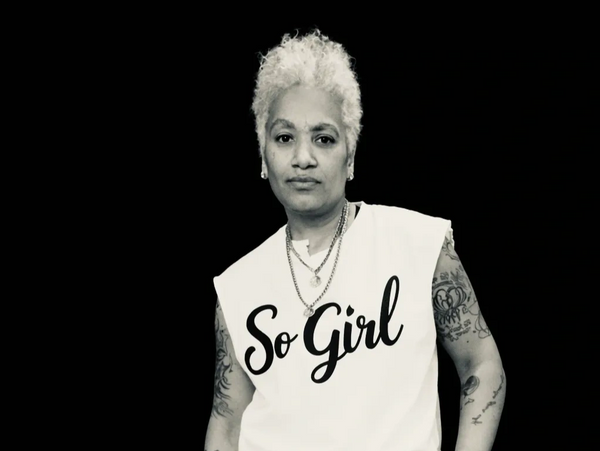 Confident person with white hair wearing a 'So Girl' shirt and tattoos.