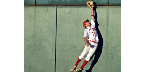 Baseball player in the outfield jumping and reaching to catch a ball at the wall.