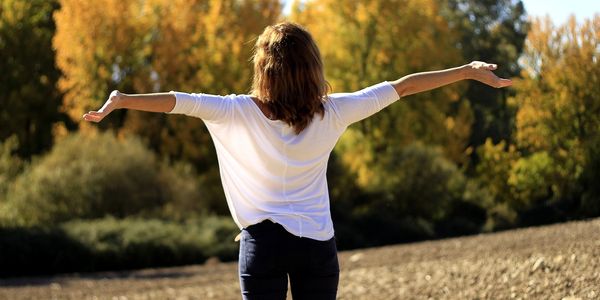 Person with arms out, looing up to wards the sun in a field with trees