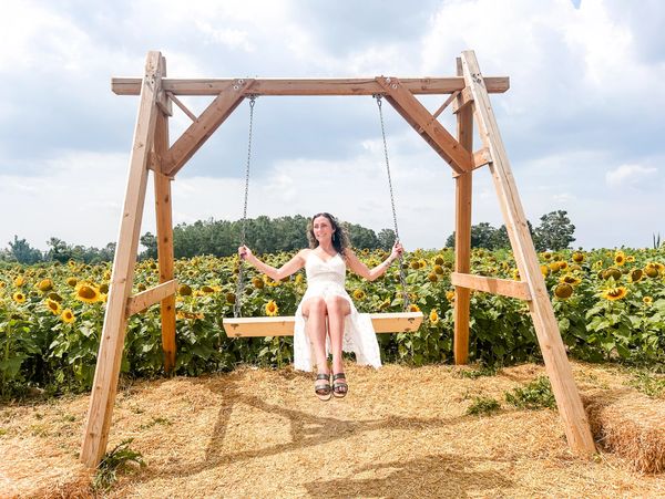 Woman in white dress sitting on a wooden swing in a sunflower field.